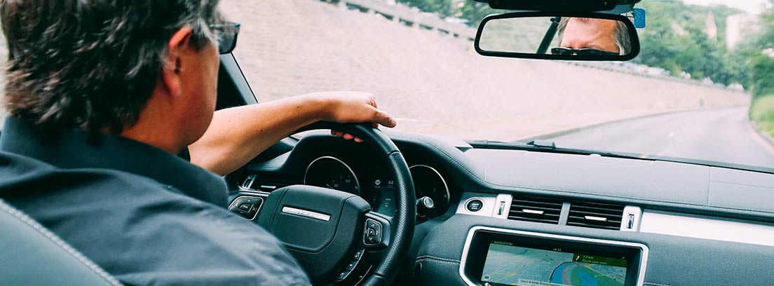 Hombre de espaladas dentro de un coche con una mano sobre el volante.