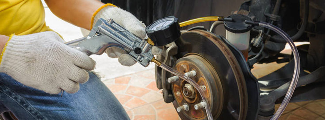 Persona de rodillas junto a rueda coche con tubo conectado al purgador.